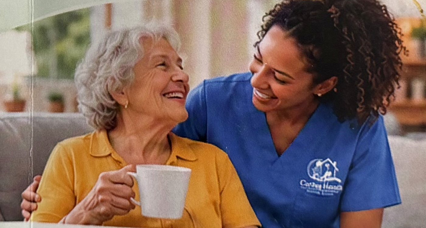 A caregiver and a senior woman laughing together over coffee